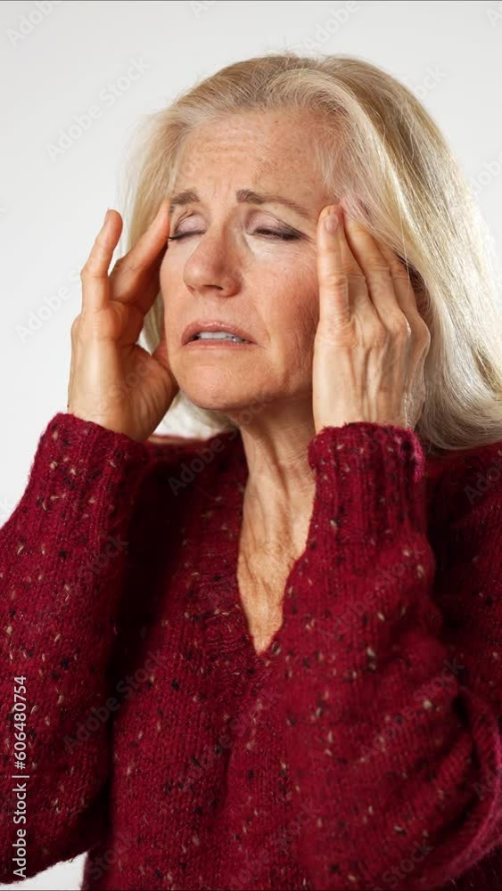 Vertical video portrait of sick tired exhausted displeased elderly gray-haired woman lady 50s 60s years old put hands on head rubs temples with headache isolated on solid white background studio.