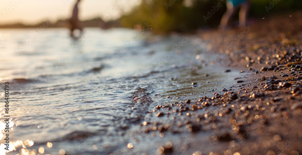 Close-up of the shore of a lake or river made of small stones against a colorful sunset background. A beautiful place in nature for family holidays and swimming. Close-up of the shore of a lake or river made of small stones against a colorful sunset background. A beautiful place in nature for family holidays and swimming.