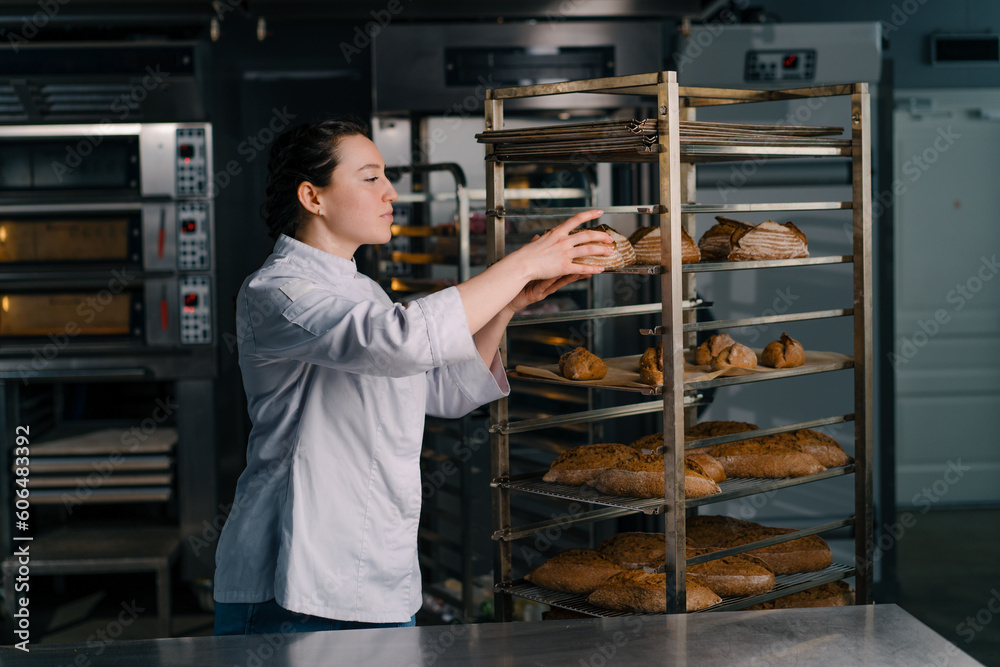 attractive female baker takes freshly baked fragrant bread from the shelf sniffs it checks its quality bakery professional kitchen baking