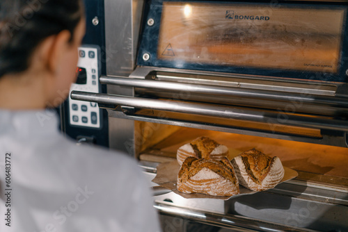 female baker takes out freshly baked fresh bread from the oven and puts it on the shelf in the kitchen of the bakery Culinary profession