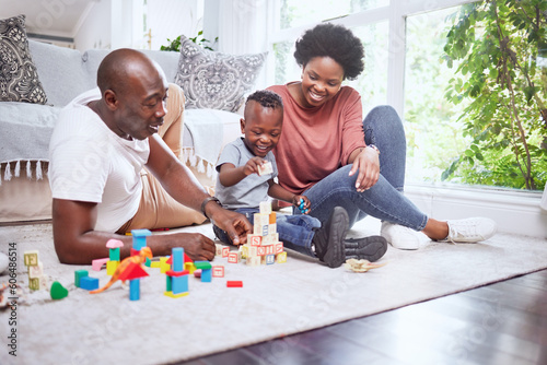 Toys, building blocks and black family playing on a living room floor happy, love and bonding in their home. Child development, learning and kid with parents in a lounge with alphabet, shape and game