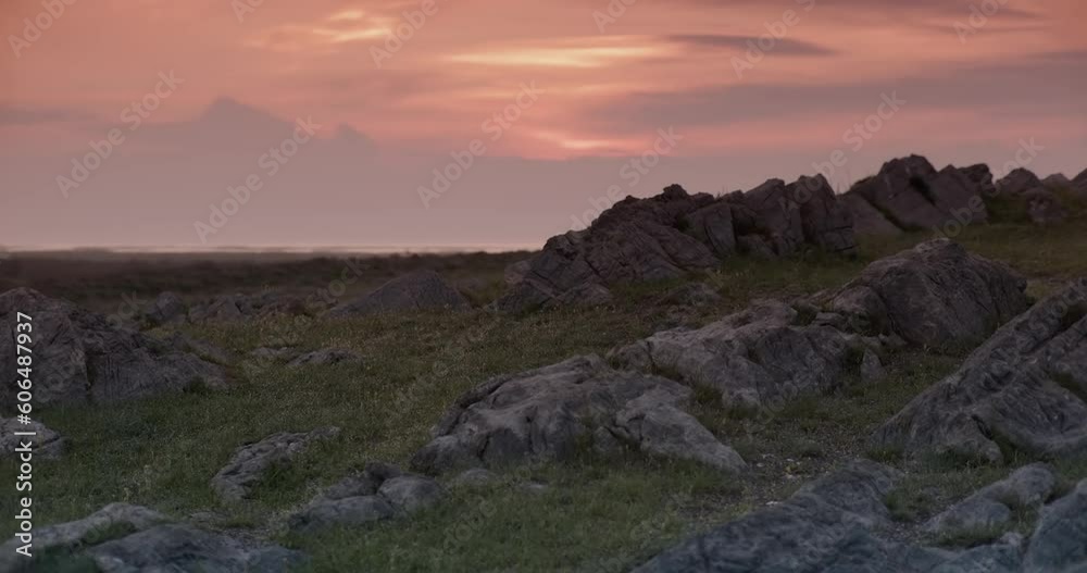 View of rocky hills with bushes and grass against a cloudy sunset sky View of rocky hills with bushes and grass against a cloudy sunset sky