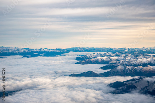 View of the snow covered Andes Mountains, surrounded by clouds,  through the window of an airplane at sunrise © phjacky65