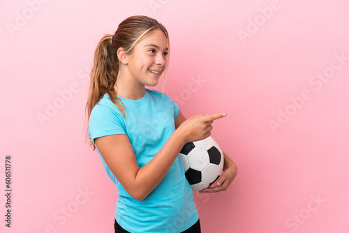 Little football player girl isolated on pink background pointing finger to the side and presenting a product