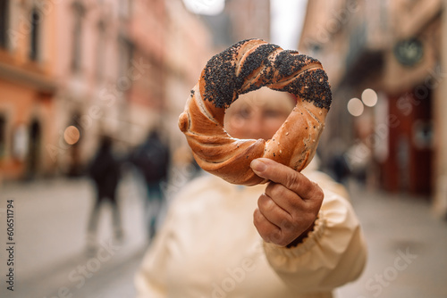 Senior woman holding prezel, traditional polish snack against old city center view in Krakow. 