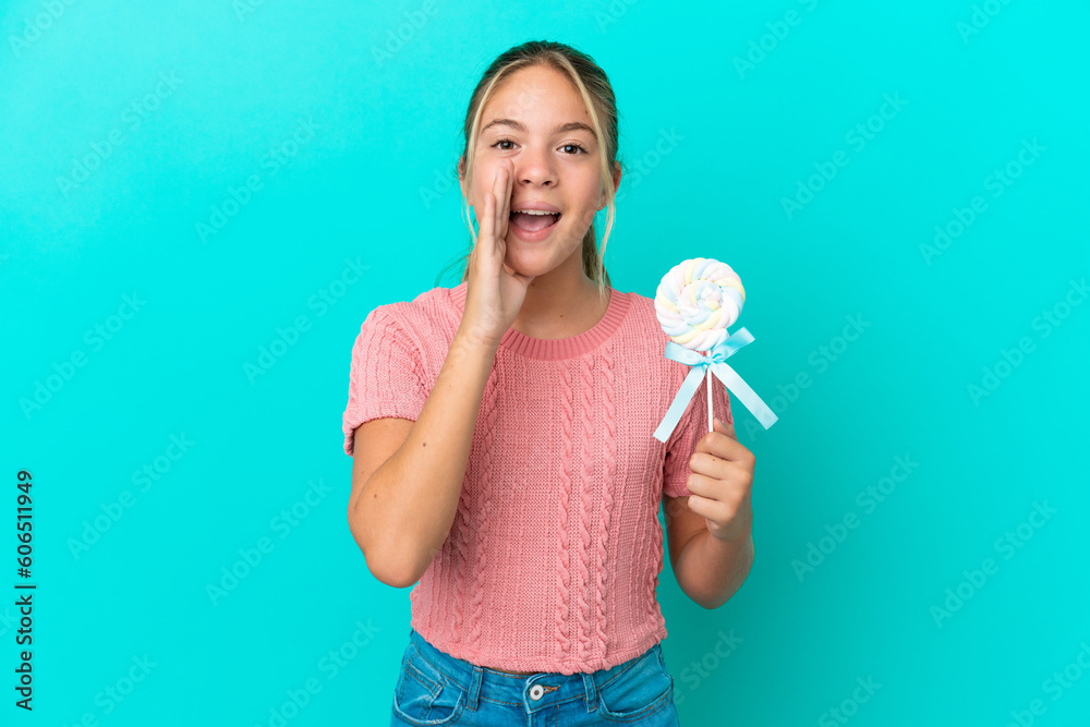 Little Caucasian girl holding a lollipop isolated on blue background shouting with mouth wide open Little Caucasian girl holding a lollipop isolated on blue background shouting with mouth wide open