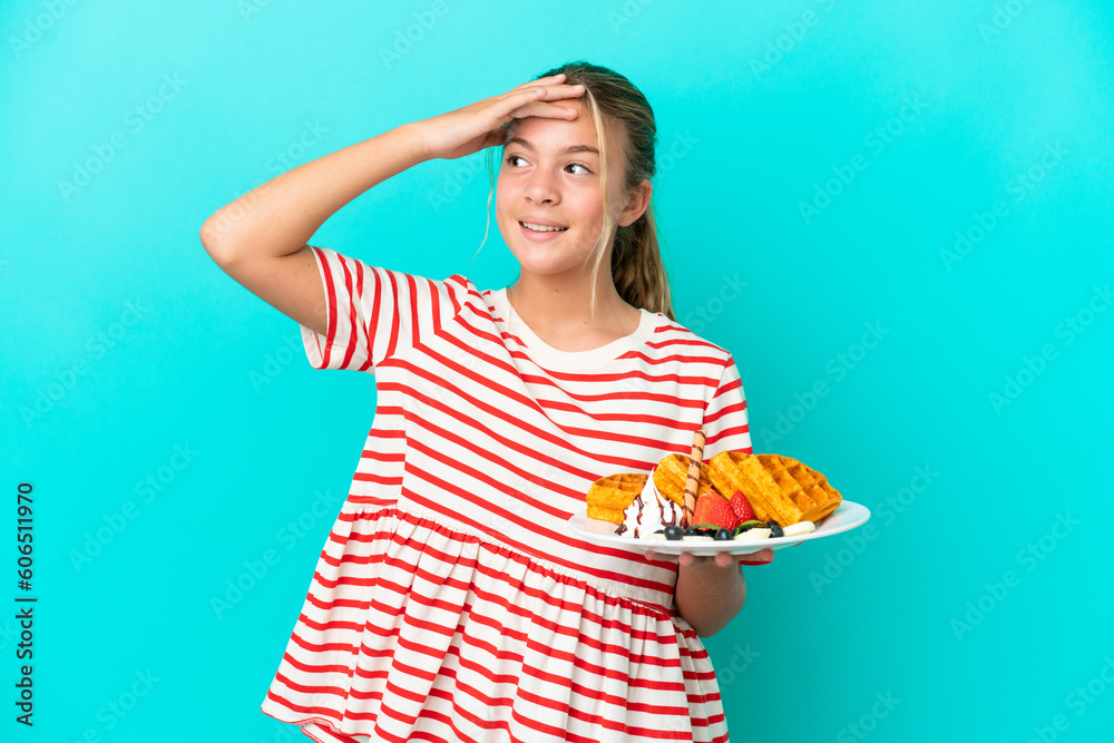 Little caucasian girl holding waffles isolated on blue background smiling a lot Little caucasian girl holding waffles isolated on blue background smiling a lot