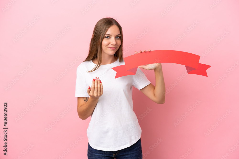Young Lithuanian woman isolated on pink background holding an empty placard and doing coming gesture