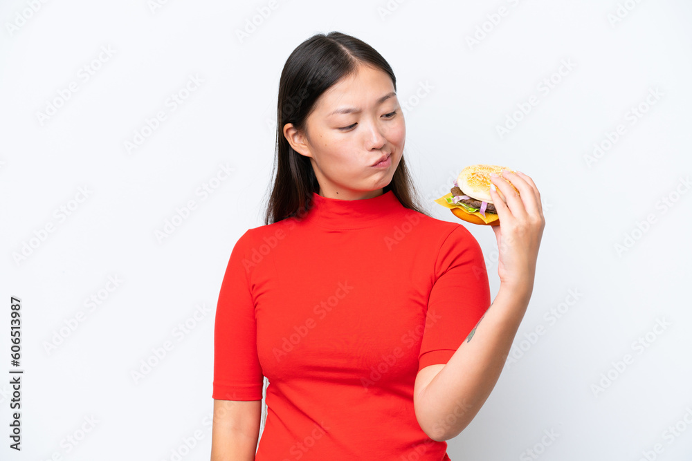 Young Asian woman holding a burger isolated on white background with sad expression Young Asian woman holding a burger isolated on white background with sad expression