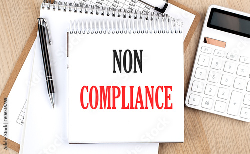 NON COMPLIANCE is written in white notepad near a calculator, clipboard and pen. Business concept photo