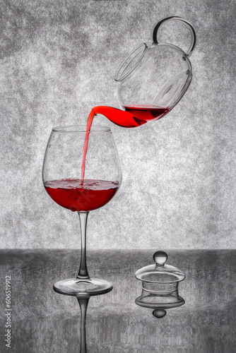 Pouring red liquid from a teapot into a glass on a gray background