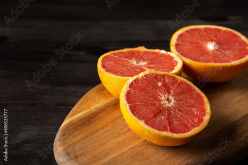 Top view of cut grapefruits on wooden board and dark table, horizontal, with copy space