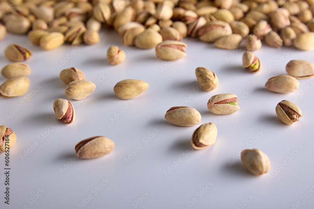 A lot of healthy, delicious, high-calorie, nutritious pistachio nuts in a hard yellow shell are scattered on a white background. Roasted pistachios in the shell on the background of a white table A lot of healthy, delicious, high-calorie, nutritious pistachio nuts in a hard yellow shell are scattered on a white background. Roasted pistachios in the shell on the background of a white table