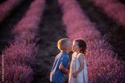 Close-up portrait of little girl kissing boy on cheek in purple lavender field. Loving cute couple