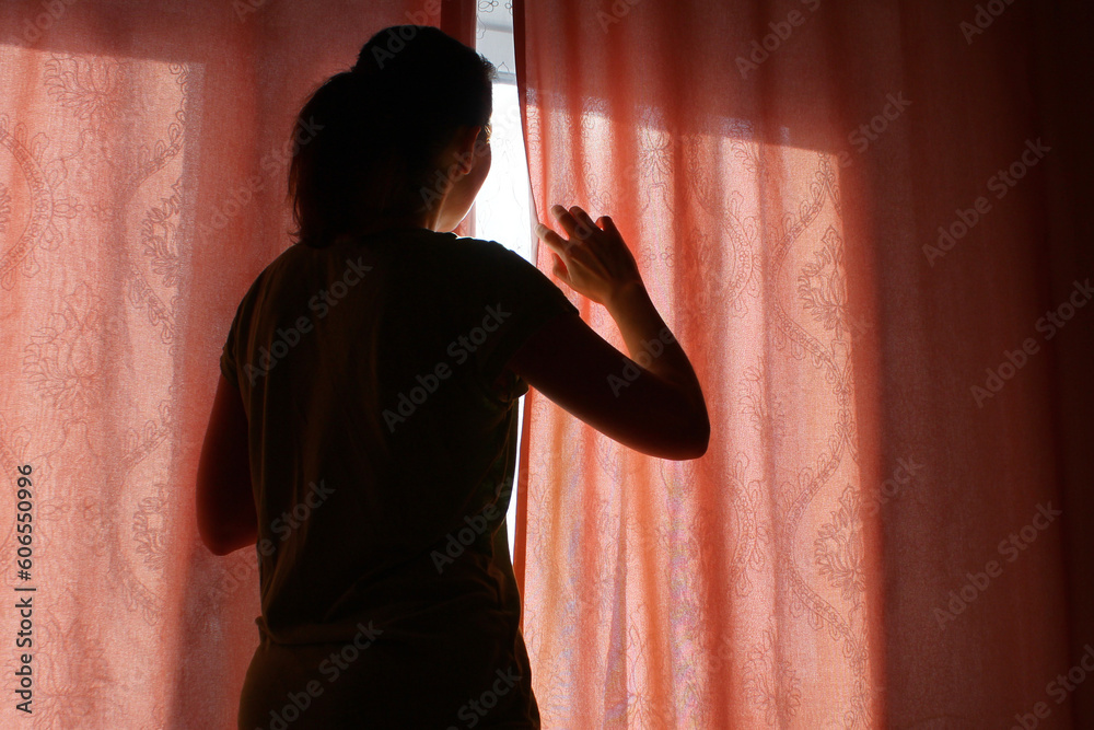 Φωτογραφία the woman behind the curtain cautiously looks out of the window into the street