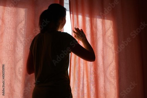 Fotografie the woman behind the curtain cautiously looks out of the window into the street
