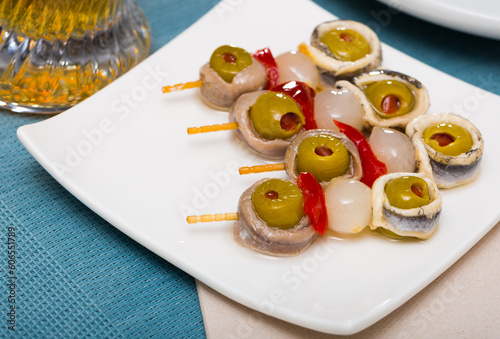 Piquant tapa of marinated anchovies fillet rolls with stuffed olives, onion and paprika on skewers
