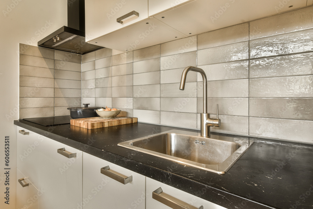 a kitchen with black counter tops and white tiles on the wall behind it is a stainless fauced sink a kitchen with black counter tops and white tiles on the wall behind it is a stainless fauced sink