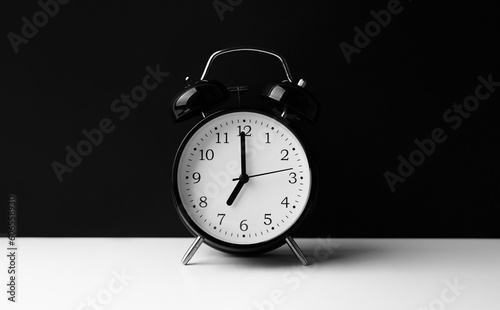 Black alarm clock on white table on black background.