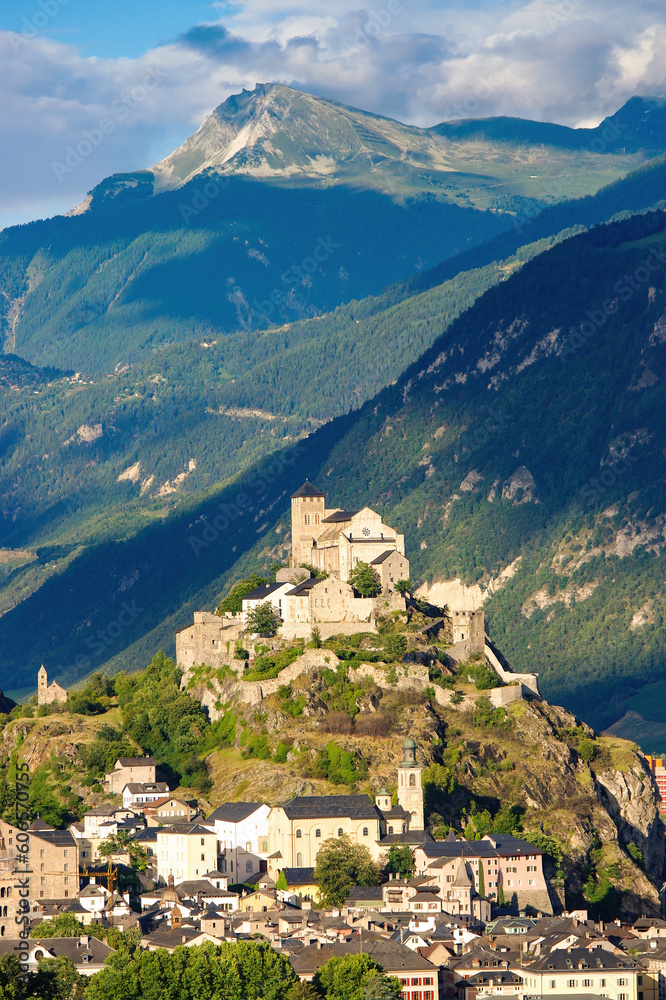Fototapeta premium Majestic Valere Basilica perched atop a stone hill, the basilica overlooks the charming old city center of Sion, Switzerland. Dramatic backdrop with towering mountains
