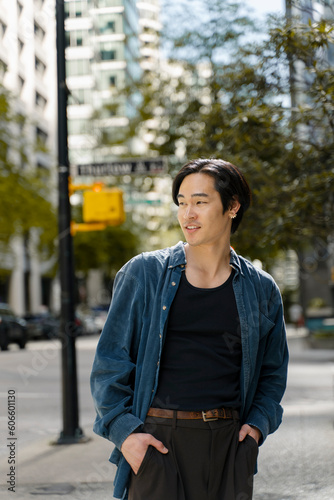 Portrait of attractive smiling asian man holding hands in pockets wearing stylish casual outfit looking away standing on the street © Maria Vitkovska