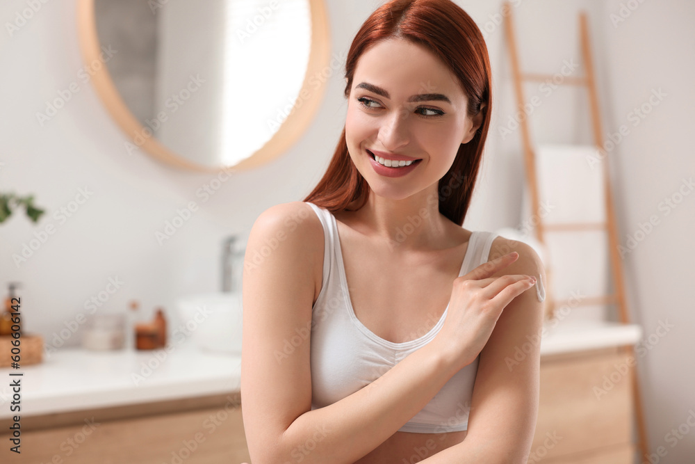 Beautiful young woman applying body cream onto shoulder in bathroom, space for text Beautiful young woman applying body cream onto shoulder in bathroom, space for text