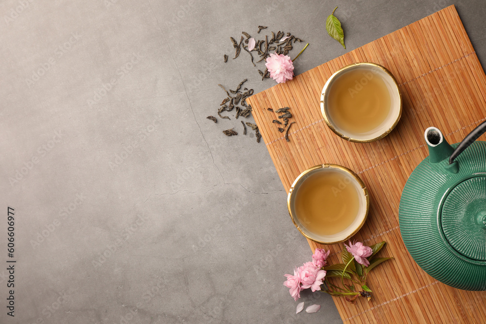 Traditional ceremony. Cups of brewed tea, teapot and sakura flowers on grey table, flat lay with space for text - obrazy, fototapety, plakaty 