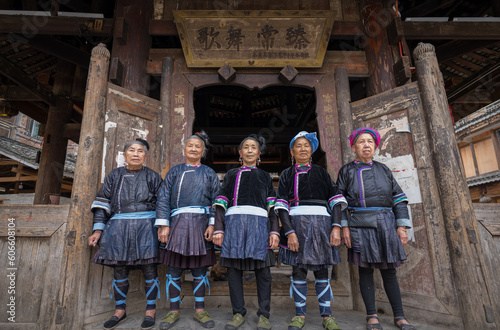 A singing group of 5 ethnic Kam women stand in front of the wooden drum tower in Xiaohuang village, Congjiang county, Guizhou, China.