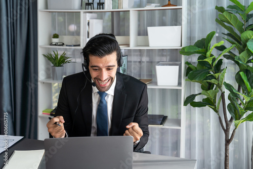 Фотография Male call center operator or telesales representative siting at his office desk wearing headset and in conversation with client providing customer service support or making persuasive sale