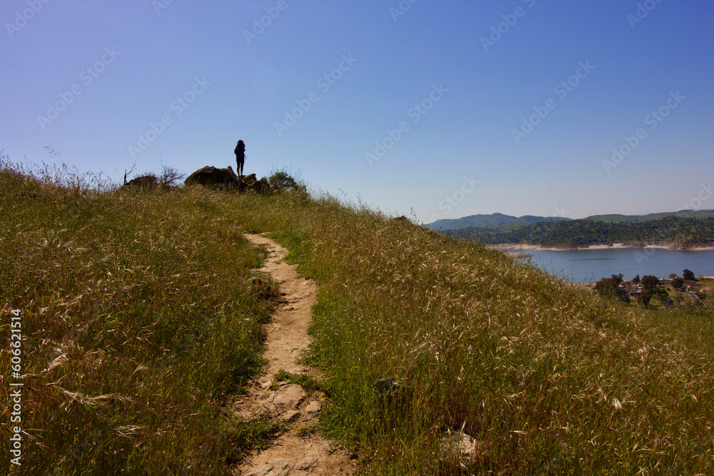 a lone female hiker stops at the top of buzzards roost trail to look out at millerton lake at millerton lake state park, fresno county, california