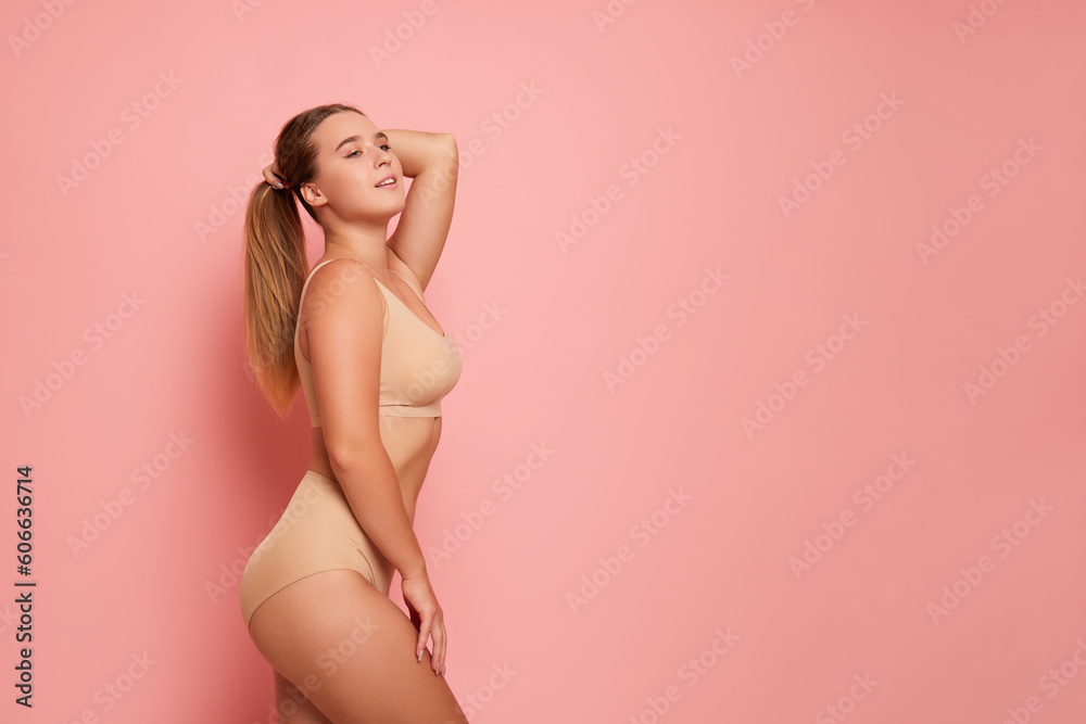 Cute girl with long hair wearing beige colour underwear poses on pink background in sexy pose with one hand on her hair, other on her hip, body comfort concept, copy space Cute girl with long hair wearing beige colour underwear poses on pink background in sexy pose with one hand on her hair, other on her hip, body comfort concept, copy space