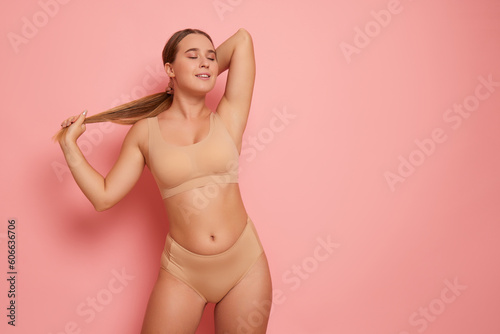 Foto Pretty girl with long hair wearing beige colour bra and panties poses on pink ba