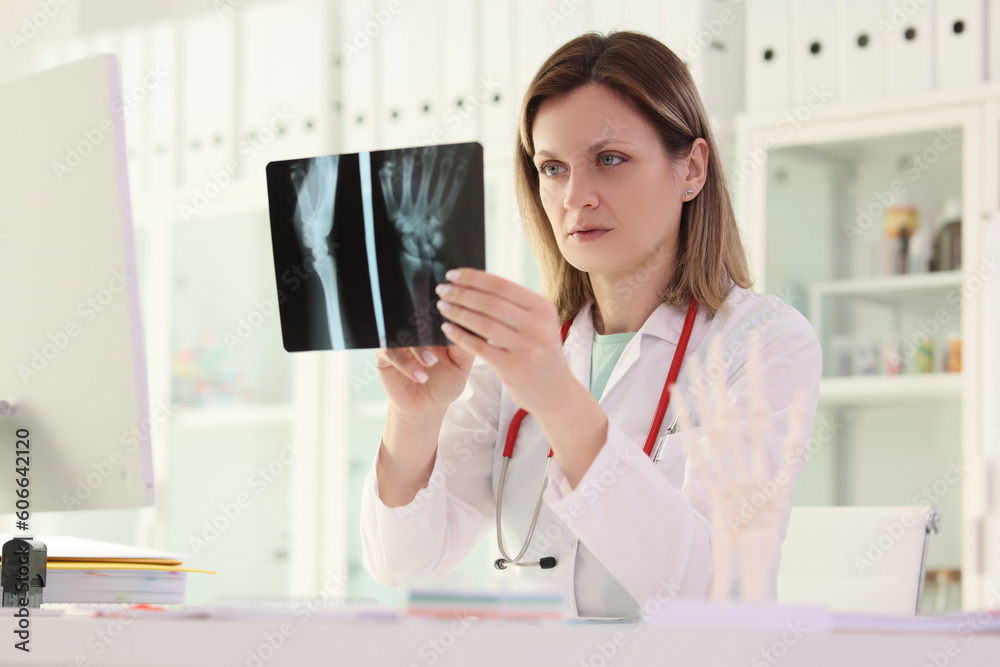 Doctor studies X-ray picture of patient arm sitting at table Doctor studies X-ray picture of patient arm sitting at table