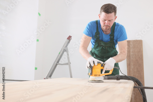 Carpenter polishes wooden desk with modern grinder machine