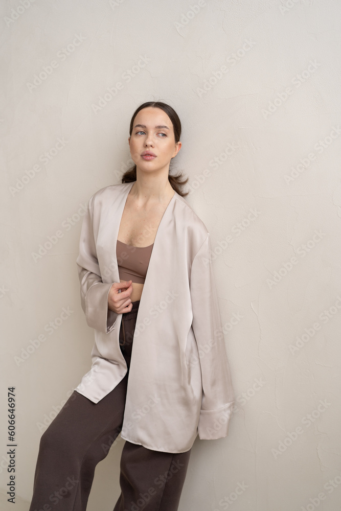 young beautiful woman posing in the studio standing in a beige cape and brown pants young beautiful woman posing in the studio standing in a beige cape and brown pants