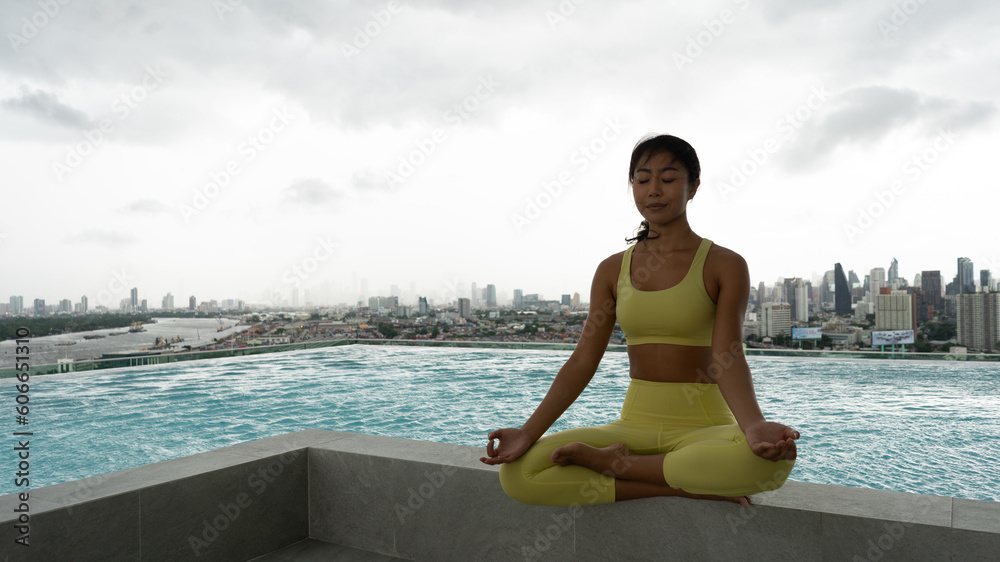 yoga meditates against modern skyscrapers. Young girl spending time fitness room on roof top of condominium doing exercises on yoga. Yoga and meditation in a modern urbanistic city. Young attractive