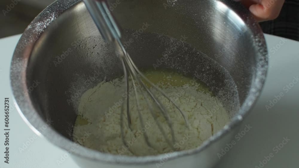 Mixing dough with hand whisk to make a pie. Hands mixing ingredients in a metal bowl on a white table. Close up. Making dough by hand with a whisk before baking. The process of making apple cake. Mixing dough with hand whisk to make a pie. Hands mixing ingredients in a metal bowl on a white table. Close up. Making dough by hand with a whisk before baking. The process of making apple cake.