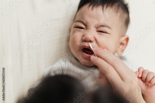 Top view, Babies crying don't like cleaning their nostrils with cotton bud. Asian baby nose care with cotton bud. Mother take care nostril cleaning of little baby. Baby care concept. photo