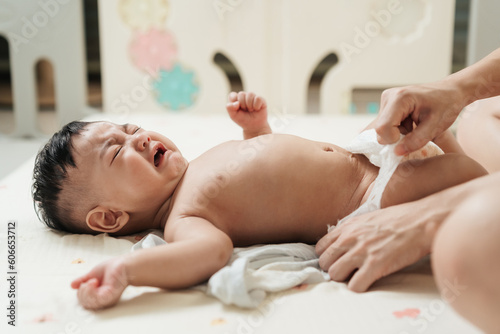 Фотография Crying Asian baby not feeling well during changing diaper by his mother