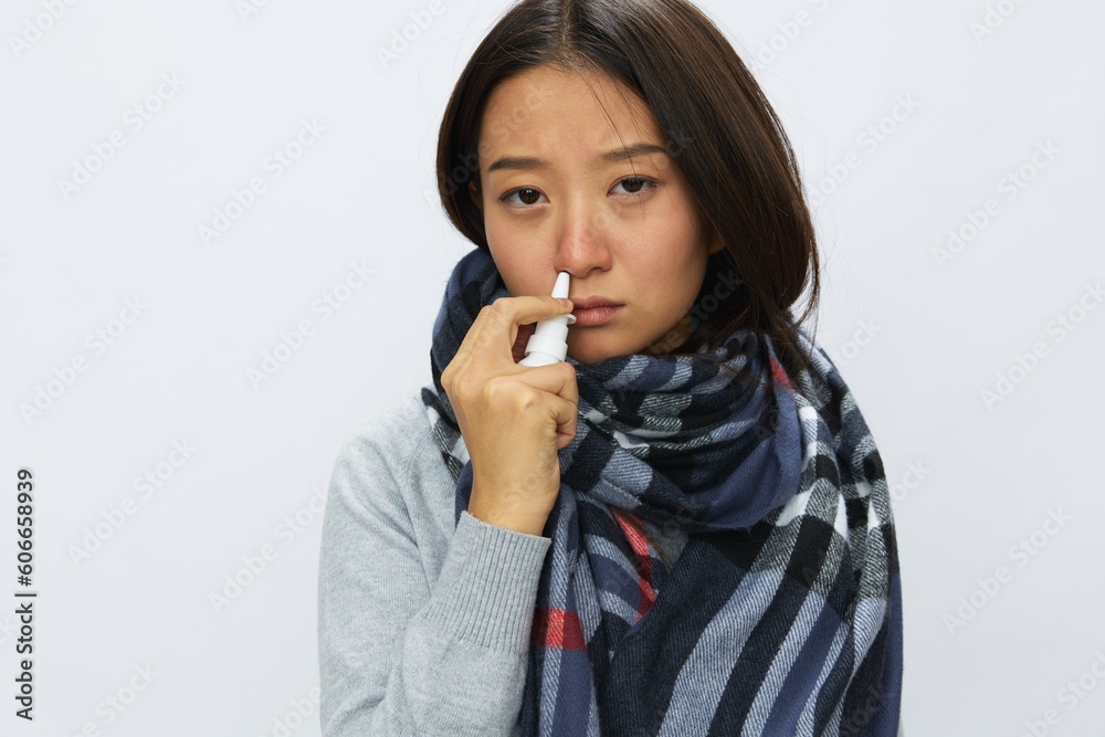 Asian woman flu cold with stuffy nose holds nasal spray and sprays nasal spray for allergies and covid 19 virus with sore throat on white background Asian woman flu cold with stuffy nose holds nasal spray and sprays nasal spray for allergies and covid 19 virus with sore throat on white background