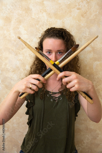 Woman holding drum sticks and paintbrushes in an x