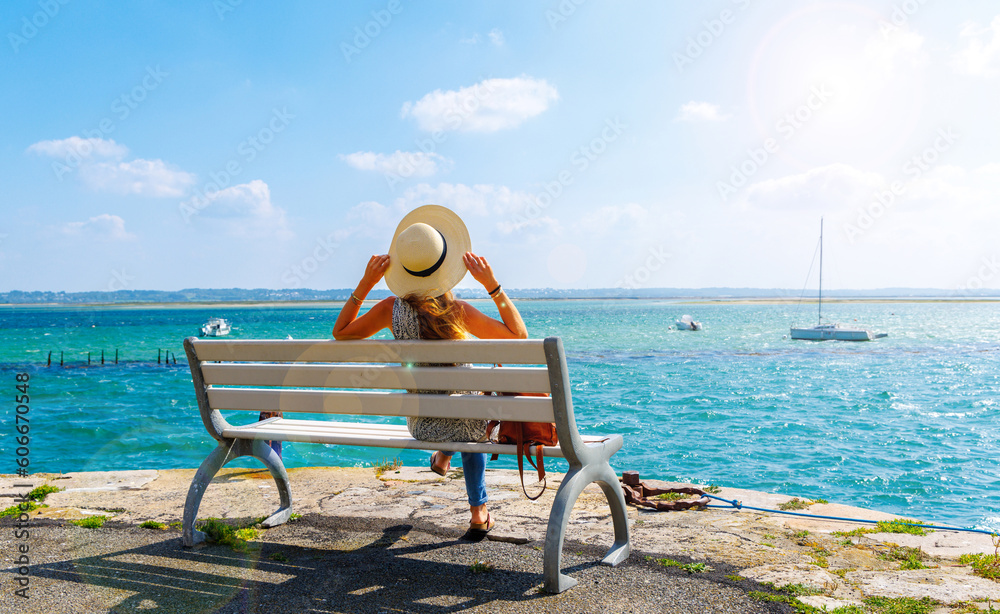 Woman sitting on a bench looking at atlantic ocean and boats- vacation, travel destination, relaxing, summer holiday ( Le croisic in France, Loire atlantic) - obrazy, fototapety, plakaty 