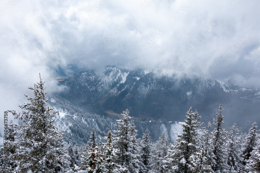Wintry view with mysterious clouds from the summit of Mount Breitenberg in the German Alps across beautiful and peaceful forests down into the valley