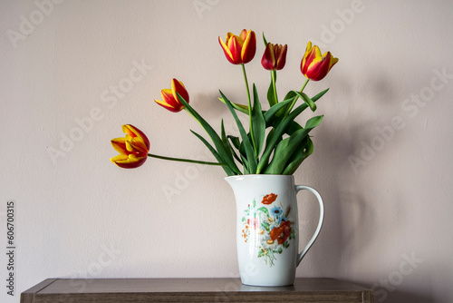 A white porcelain jug with flower print containing a bouquet of red and yellow tulips