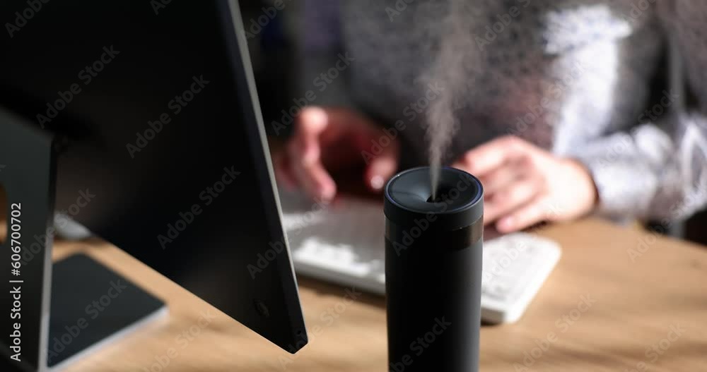 Female manager types on keyboard of computer sitting at table with aroma diffuser humidifier. Office worker enjoys scent of essential oils at workplace slow motion