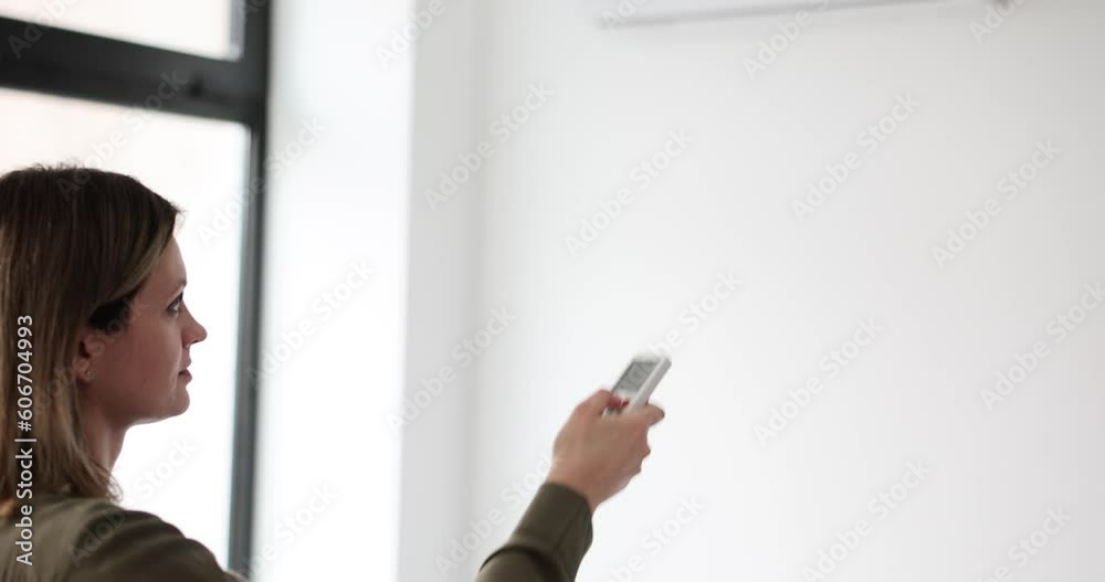 Woman stabilizes temperature with remote control standing in modern premise. Female person uses air conditioner to improve living conditions at home slow motion Woman stabilizes temperature with remote control standing in modern premise. Female person uses air conditioner to improve living conditions at home slow motion