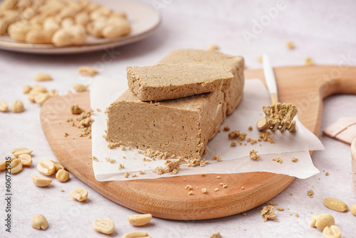 Board with tasty halva and peanuts on white background