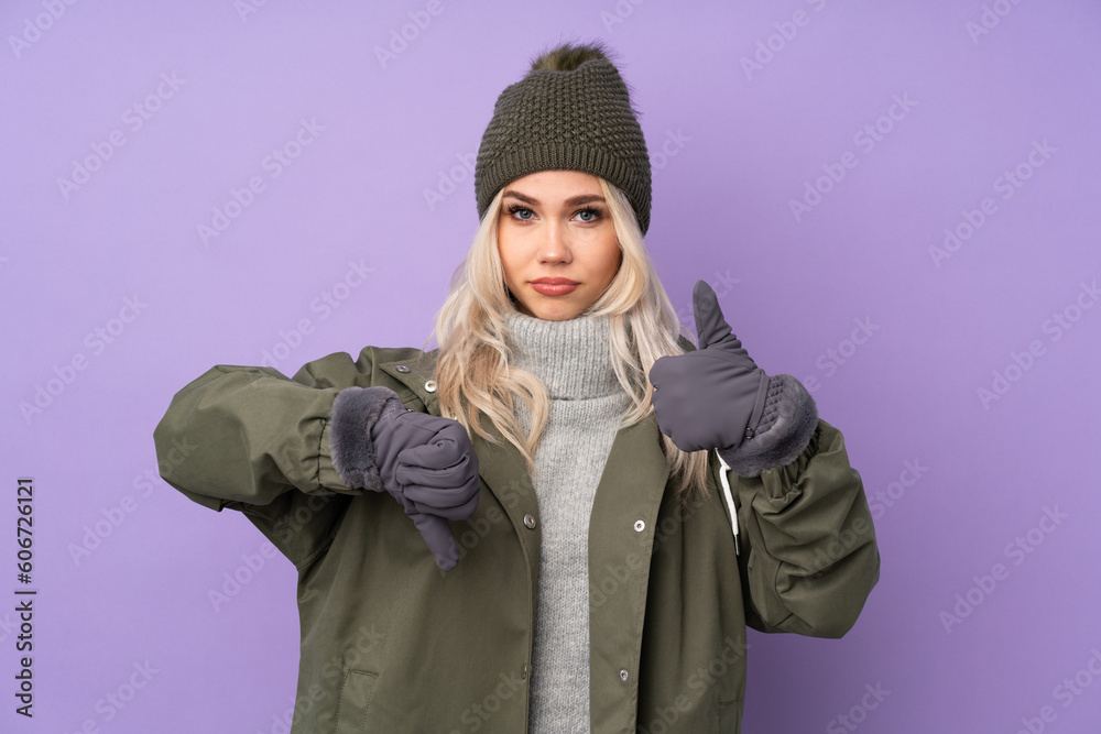 Teenager blonde girl with winter hat over isolated purple background making good-bad sign. Undecided between yes or not Teenager blonde girl with winter hat over isolated purple background making good-bad sign. Undecided between yes or not