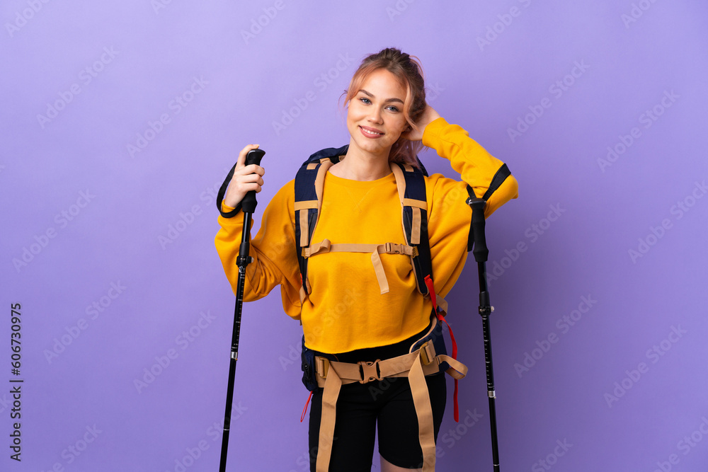 Teenager girl with backpack and trekking poles over isolated purple background laughing