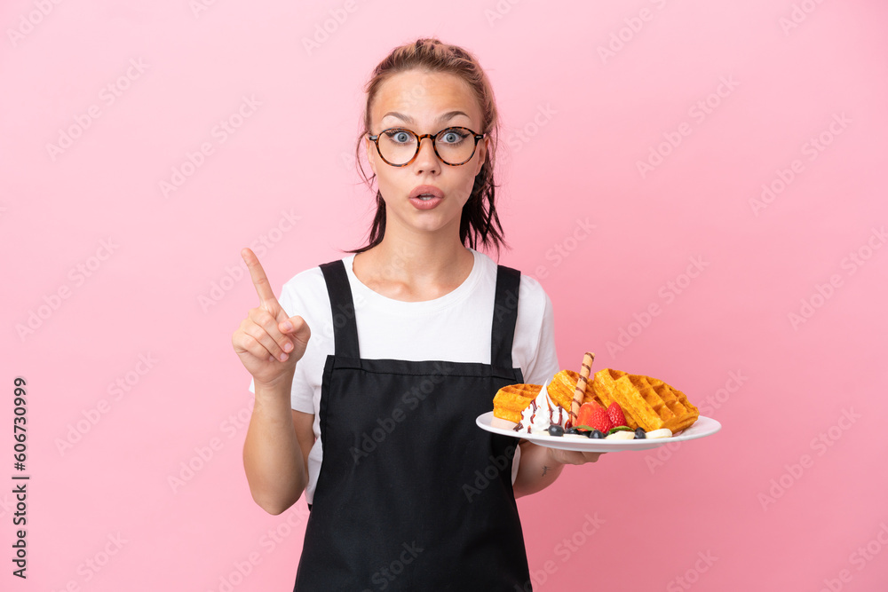 Restaurant waiter Russian girl holding waffles isolated on pink background intending to realizes the solution while lifting a finger up